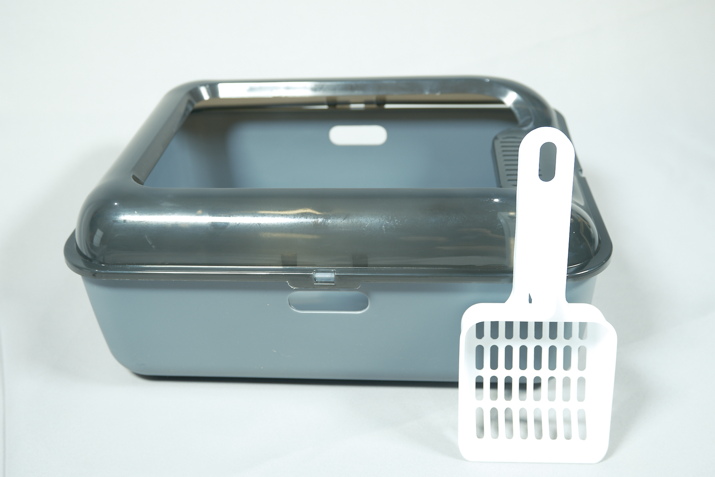 Gray pet litter box with a white scoop on a white background