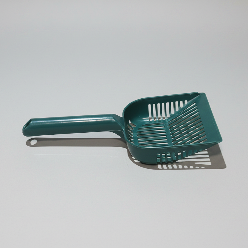 Green plastic cat litter scoop on a light gray background